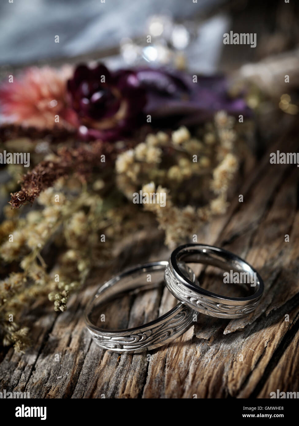 Oro bianco anelli di nozze con design celtica e selvaggio fiori secchi su sfondo rustico, matrimonio artistico still life Foto Stock