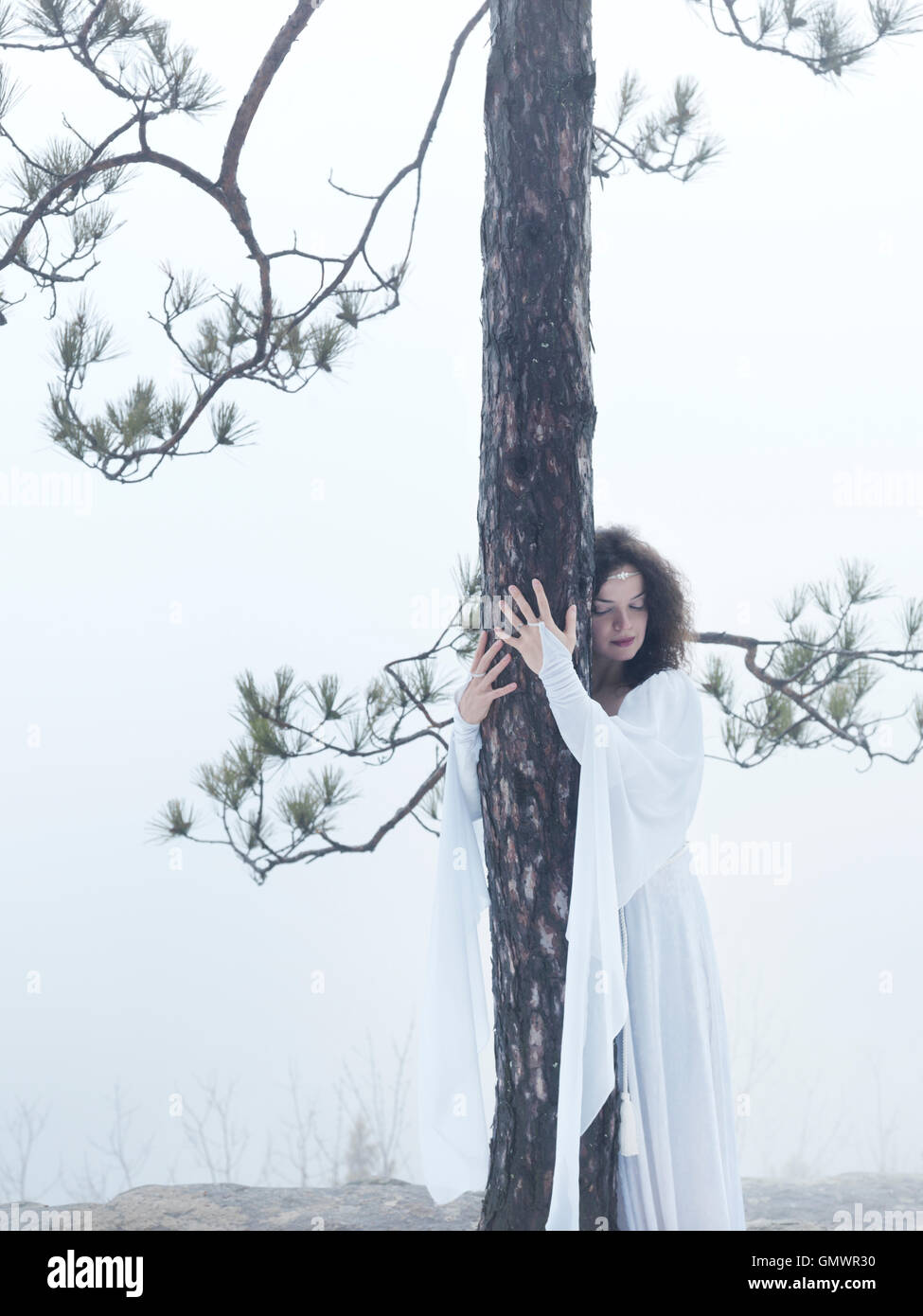 Giovane donna in abito bianco che abbraccia un pino. Ricollegare con la natura. Foto Stock