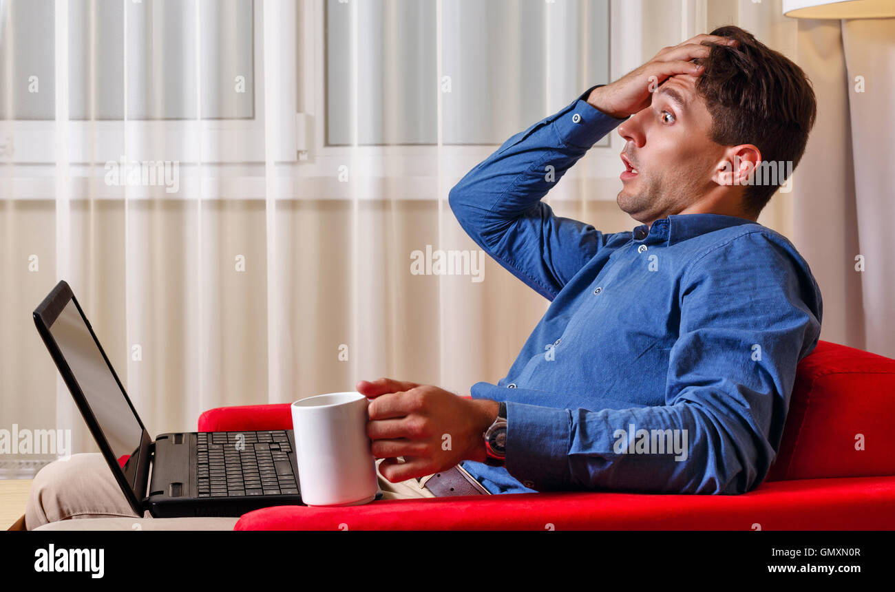 L'uomo lavora per laptop. Imprenditore tenendo una tazza di caffè e afferra la testa. Cattive notizie. Duro lavoro. Foto Stock