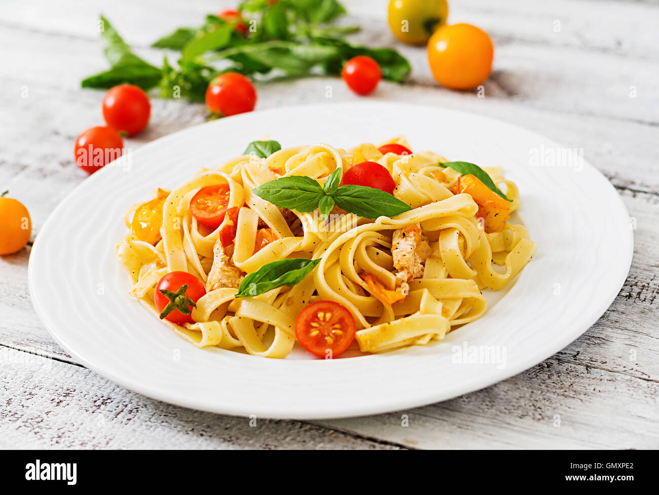 Fettuccine in salsa di pomodoro con pollo, pomodori decorate con basilico su un tavolo di legno Foto Stock