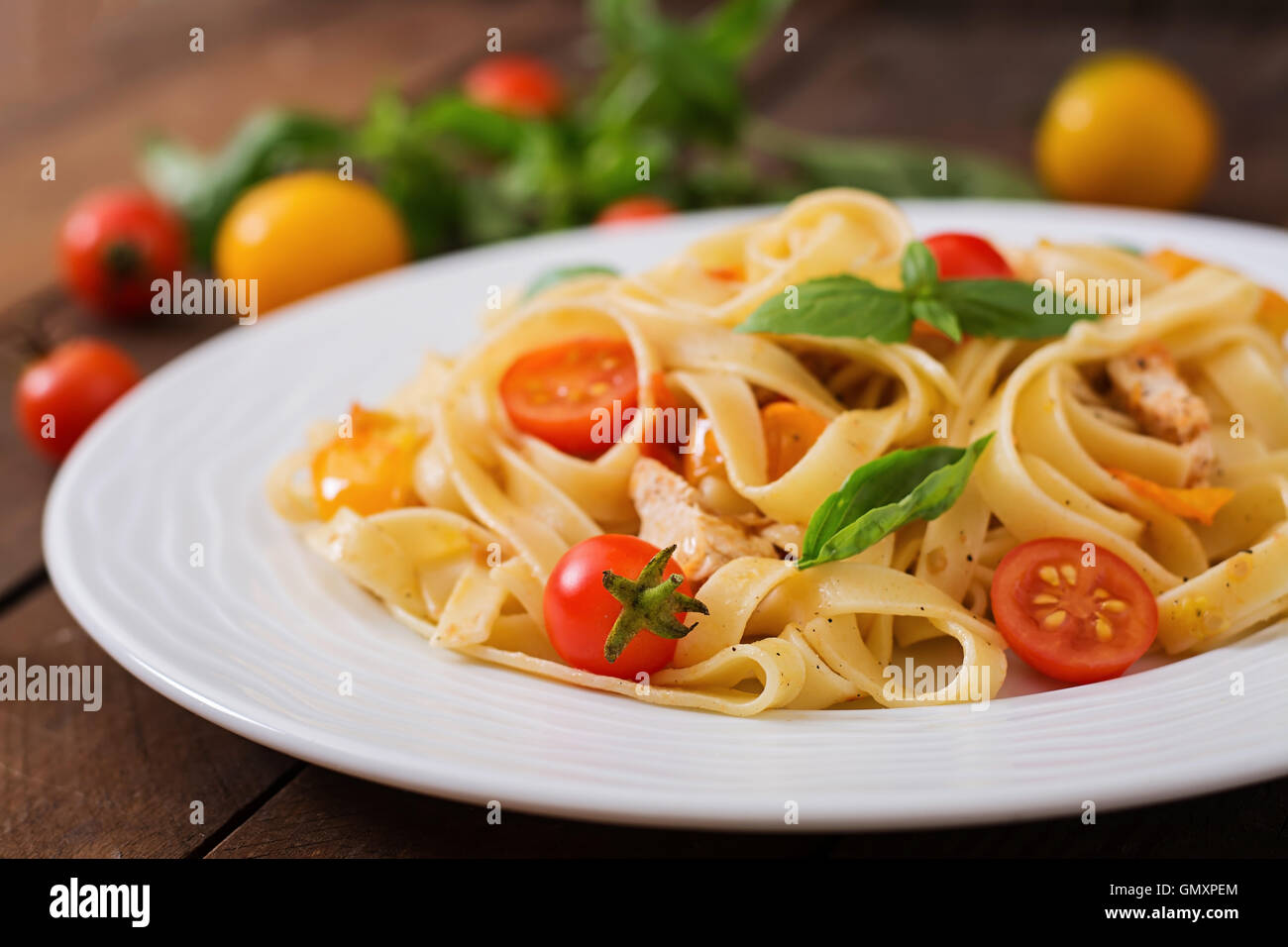 Fettuccine in salsa di pomodoro con pollo, pomodori decorate con basilico su un tavolo di legno Foto Stock