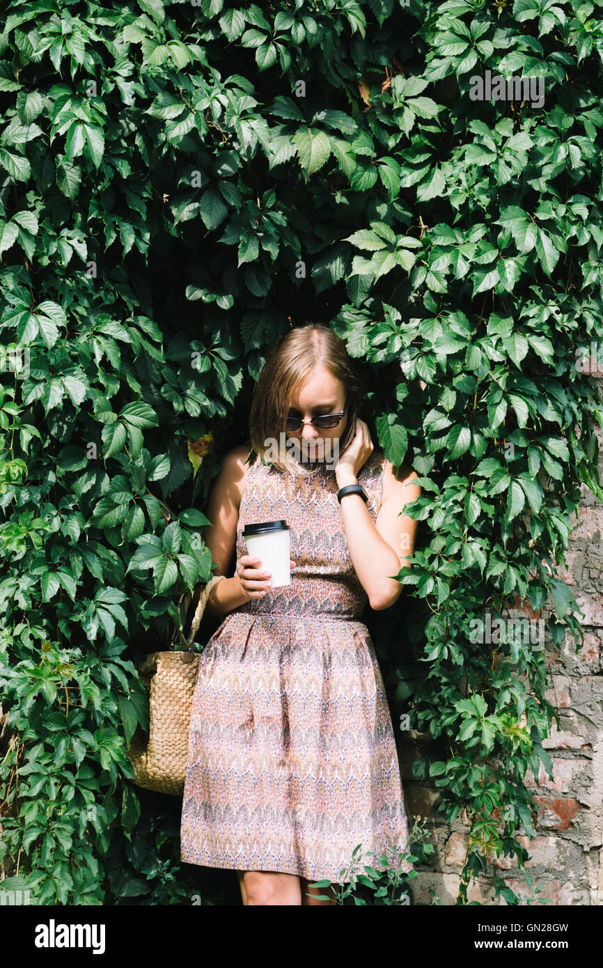 Giovane donna in abito con caffè di andare sulla siepe verde Foto Stock