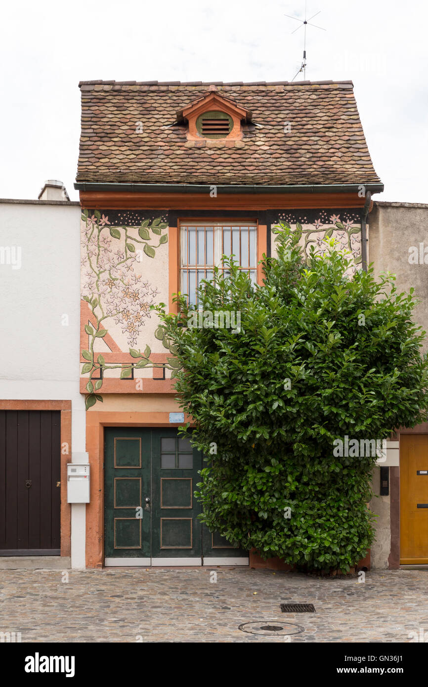 Carino piccola casa con ornamenti floreali su parete singola finestra e macchia verde nella parte anteriore. Il verde porta del garage si trova al piano terra. Foto Stock