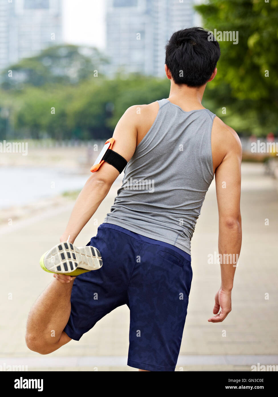 Giovani asiatici pareggiatore maschio con fitness tracker attaccata al braccio in fase di riscaldamento allungando la gamba prima dell'esecuzione. Foto Stock