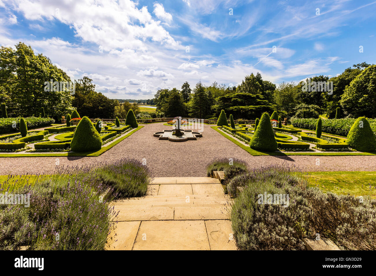 Paesaggistico giardino formale in un parco con topiaria da pietra, piantatrici e una fontana. Foto Stock