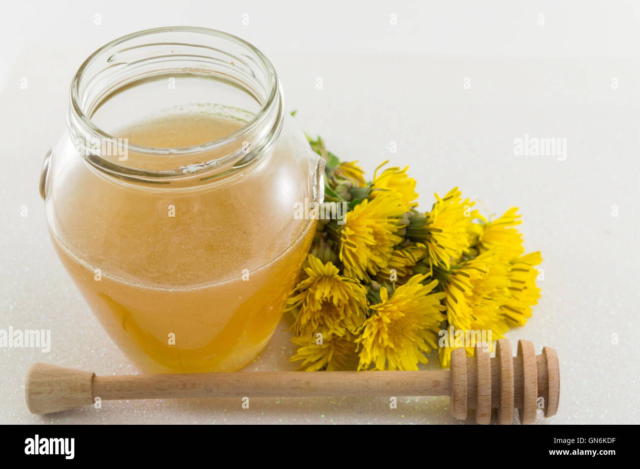 Un vasetto di miele e di tarassaco giallo su sfondo lucido Foto Stock