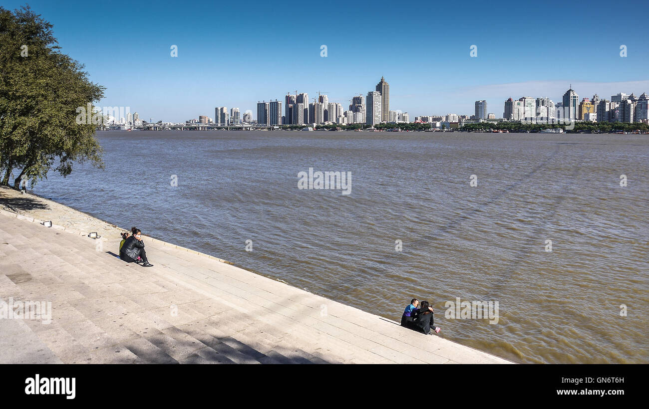 I turisti seduti a scale sulla banca del Nord, verso south bank skyline di giorno oltre il Fiume Songhua, Harbin Foto Stock