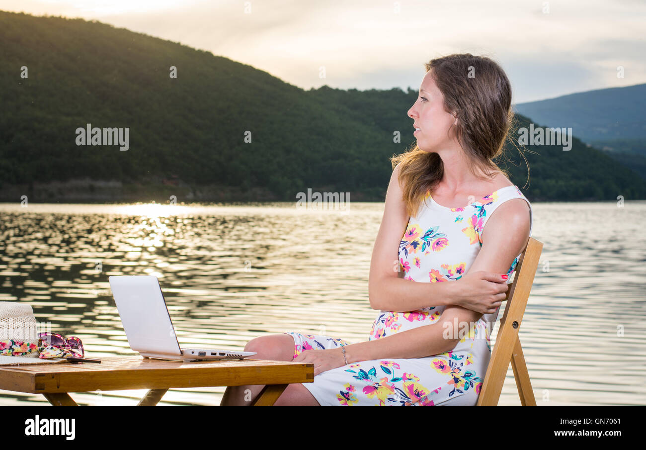 Malinconici donna avente con computer lap top in riva al lago Foto Stock