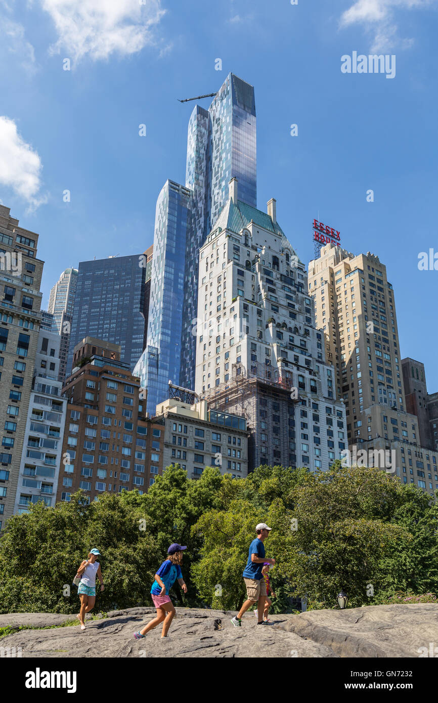 Il grattacielo residenziale uno57 torreggia su una famiglia arrampicata sulle rocce di Central Park e di altri edifici vicini sulla West 57th Street a New York City. Foto Stock Il grattacielo residenziale uno57 torreggia su una famiglia arrampicata sulle rocce di Central Park e di altri edifici vicini sulla West 57th Street a New York City. Foto Stock