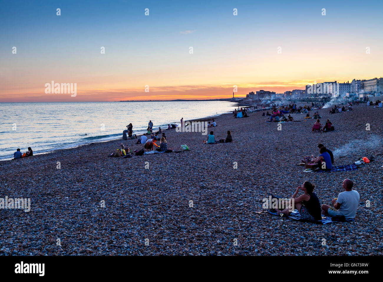 La gente seduta sulla spiaggia di Brighton al tramonto, Brighton, Sussex, Regno Unito Foto Stock