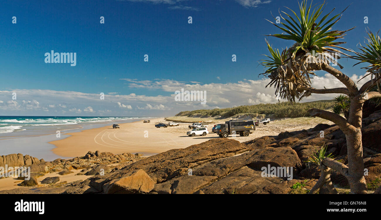 Vista panoramica del vasto 75-Mile beach ocean & rocce vicino Indian Head su Fraser Island con veicoli su strada inusuale, cielo blu Foto Stock