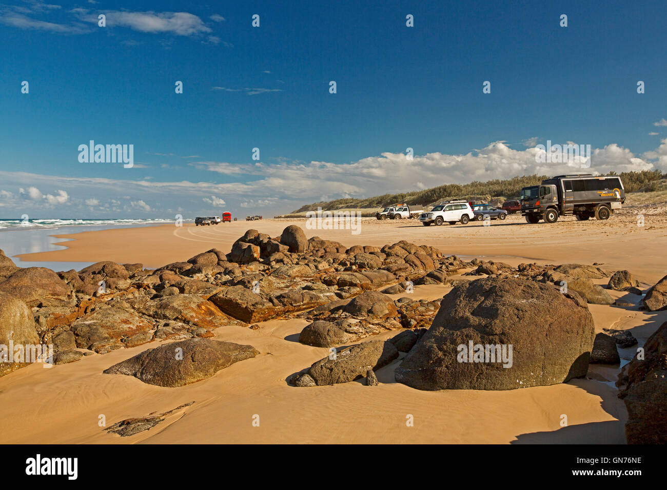 Vasto sandy 75-Mile beach ocean & rocce vicino Indian Head su Fraser Island con veicoli su autostrada insolita sotto il cielo blu Foto Stock