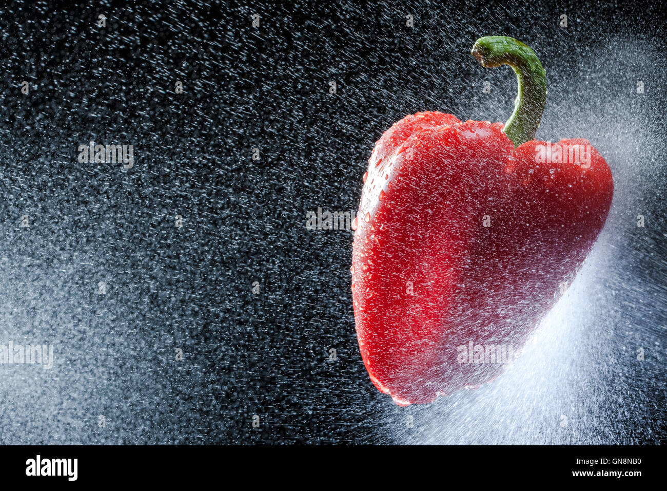 Peperone rosso in uno spray contro uno sfondo nero. Una serie di frutta e verdura in movimento. Foto Stock
