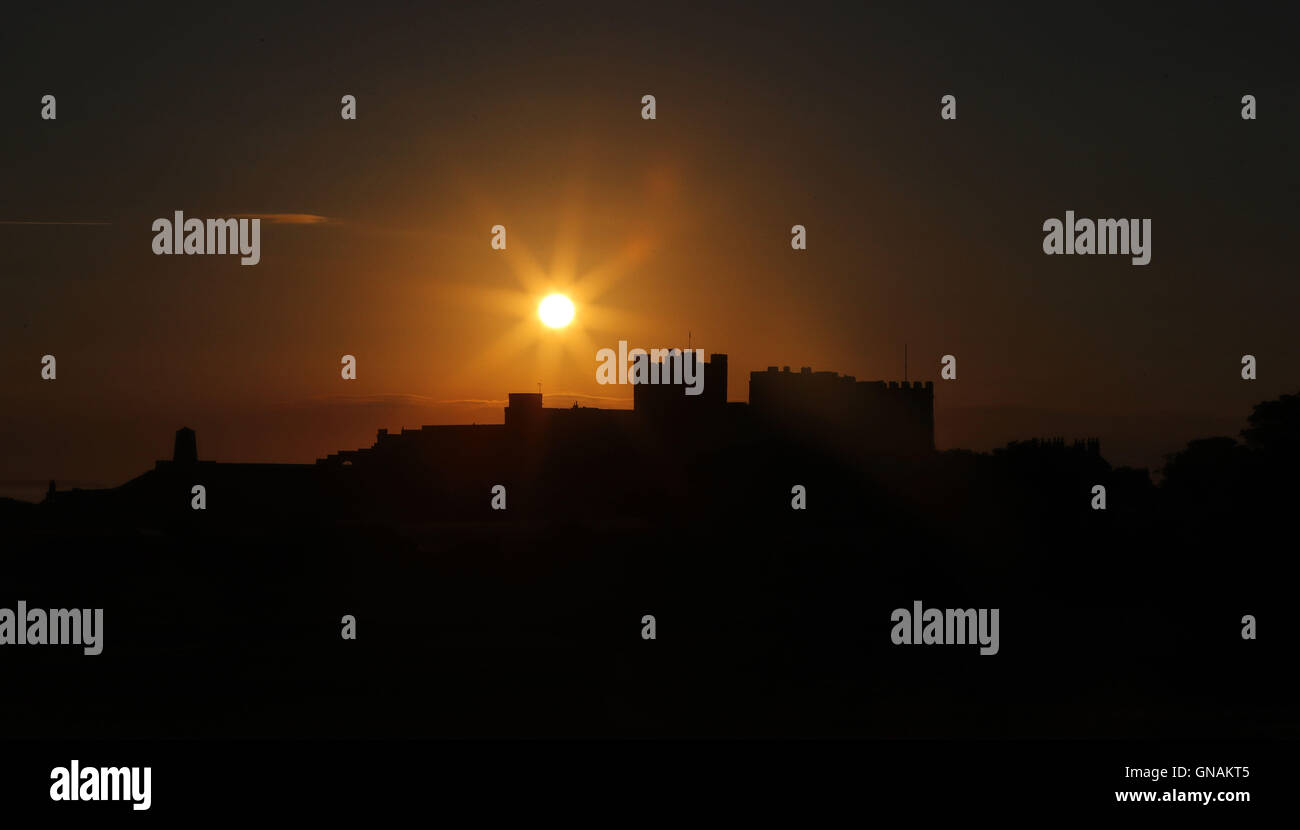 Il sole sorge oltre il castello di Bamburgh in Northumberland, come i britannici possono guardare avanti a barbecue meteo per la banca vacanza come la settimana scorsa il periodo caldo continua. Foto Stock