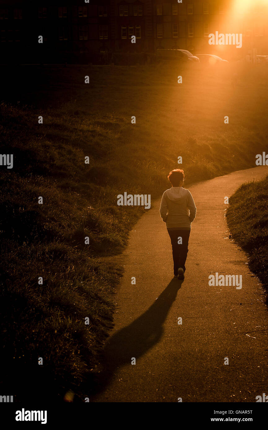 Una donna cammina lungo un percorso durante un intenso tramonto. Foto Stock
