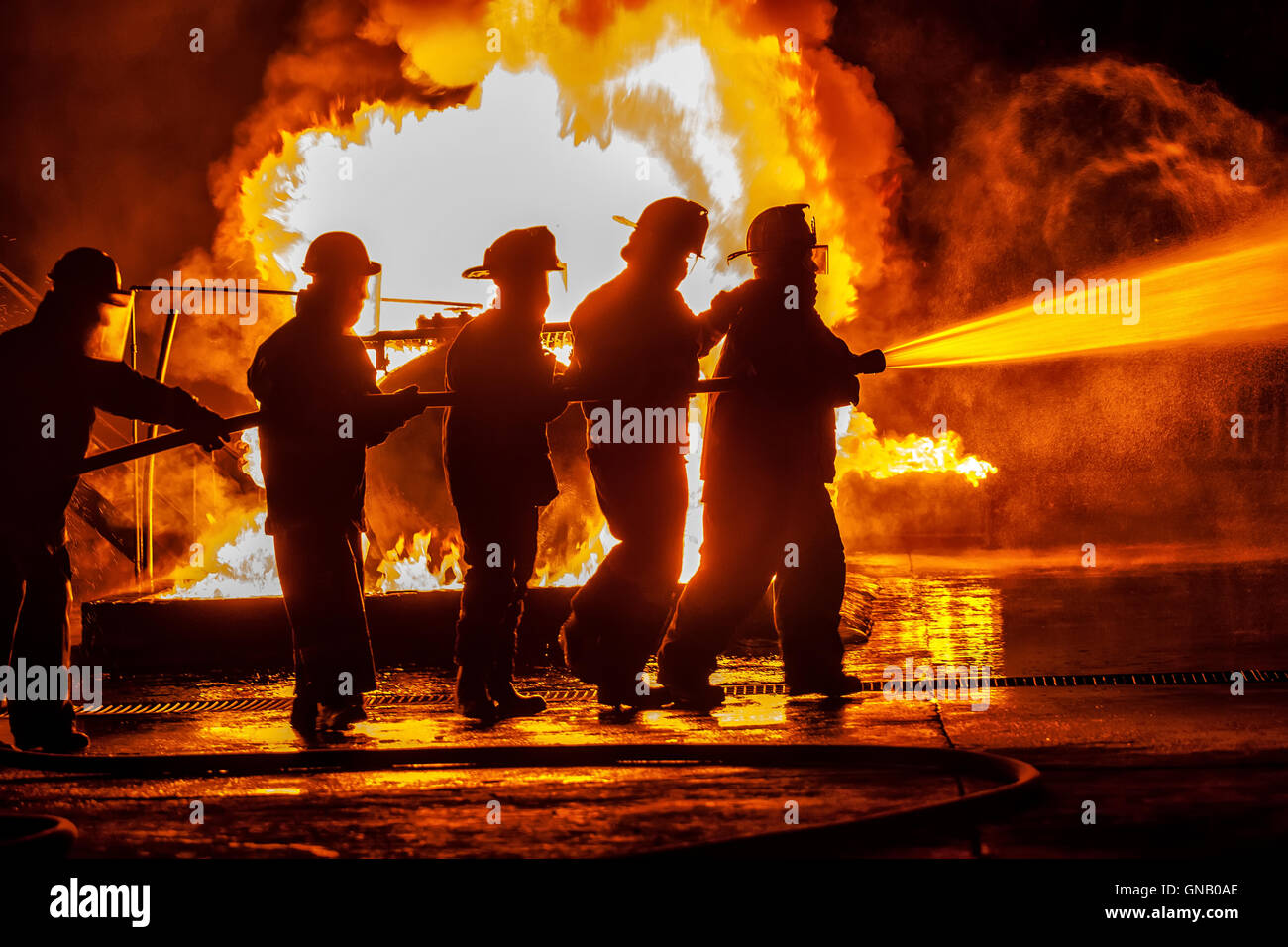 Gruppo di vigili del fuoco in movimento verso il fuoco con il tubo flessibile Foto Stock