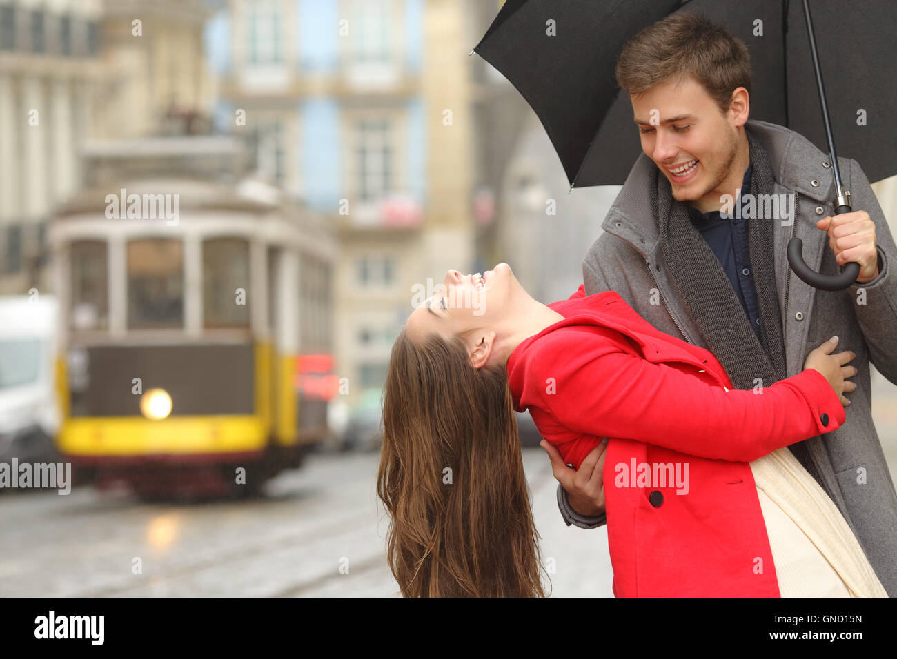 Felice coppia giocoso in love dating scherzando e ridendo nelle strade di una città vecchia in un giorno di pioggia sotto un ombrello Foto Stock