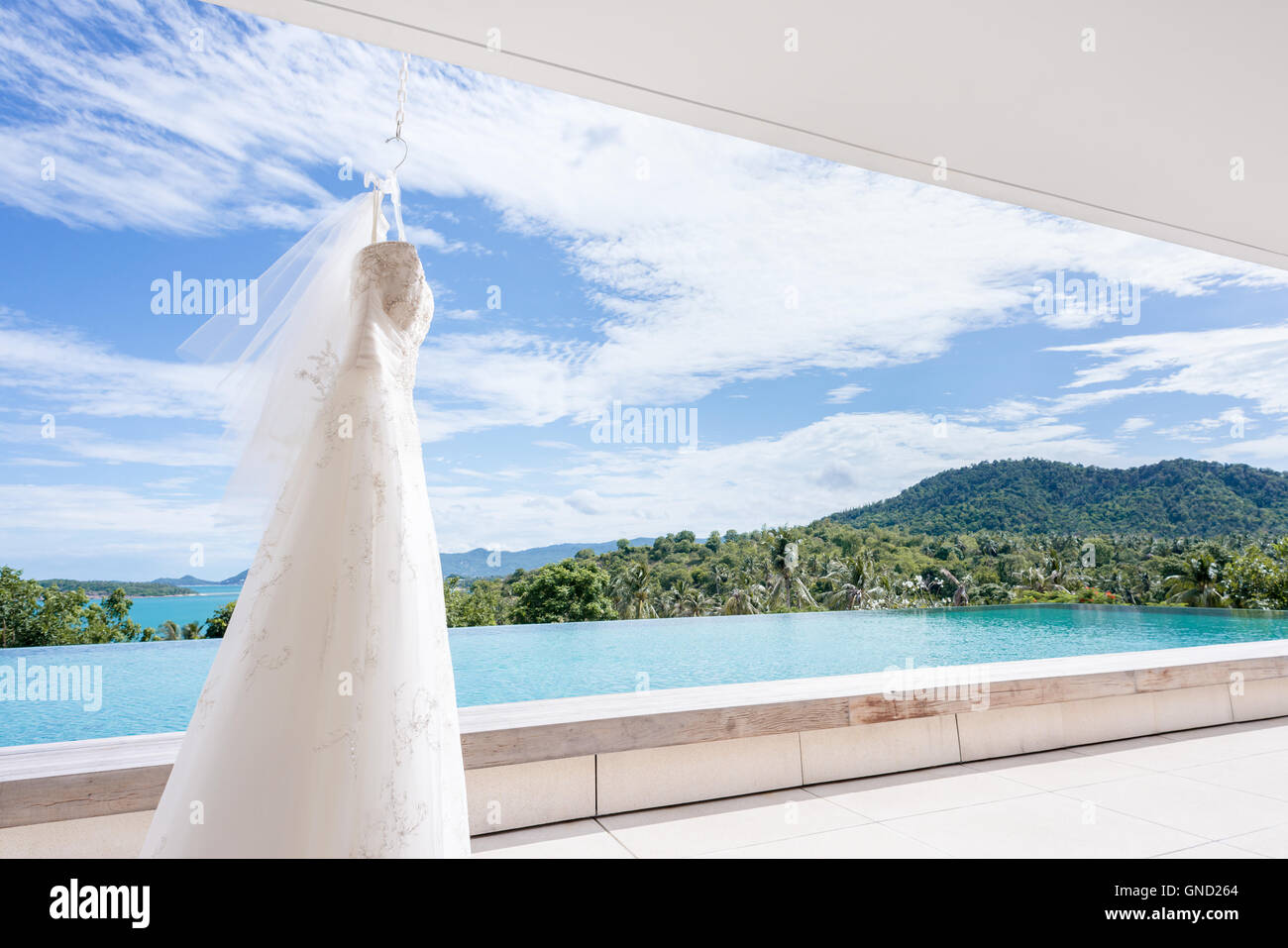 White abito da sposa appeso su una delle spalle, bel cielo azzurro sfondo. Foto Stock