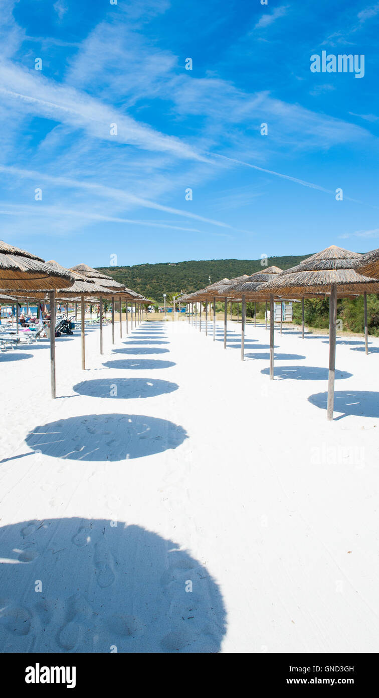 Vista verticale di ombrellone con spiaggia di sabbia bianca e verde paesaggio in background, nessuno sulla spiaggia nella giornata di sole Foto Stock