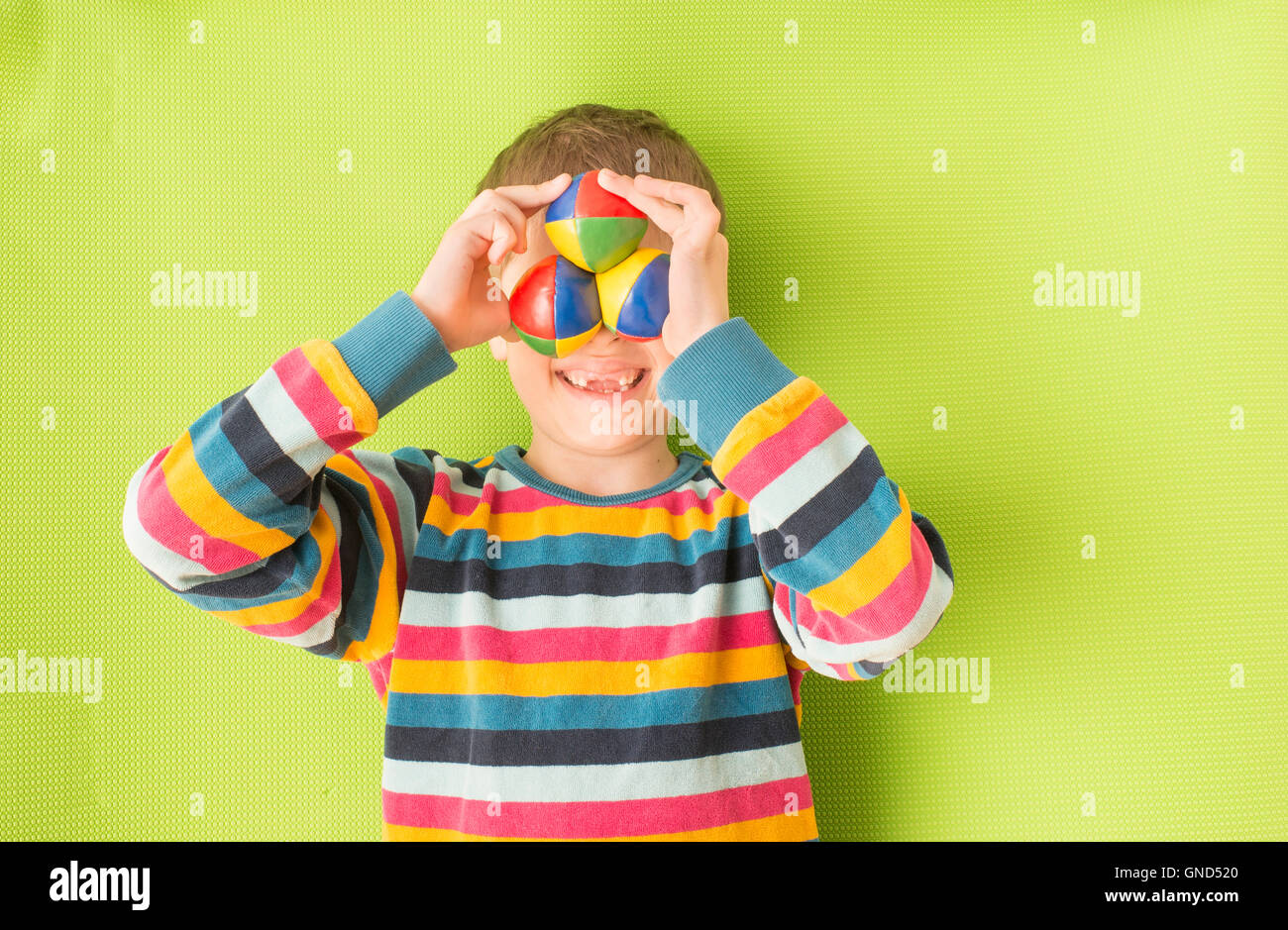 Bambina con denti mancanti di ridere. Azienda colorato juggling balls davanti agli occhi. Simpatico momento di infanzia. Foto Stock