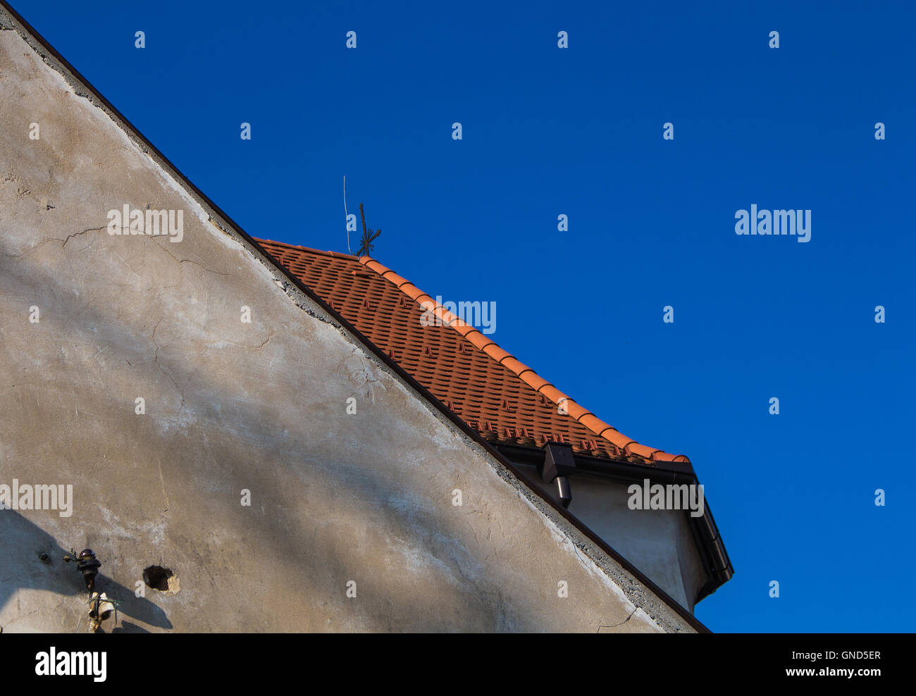 Vecchia facciata con ombre e illuminato nuovo tetto arancione dietro. Azzurro cielo. Foto Stock