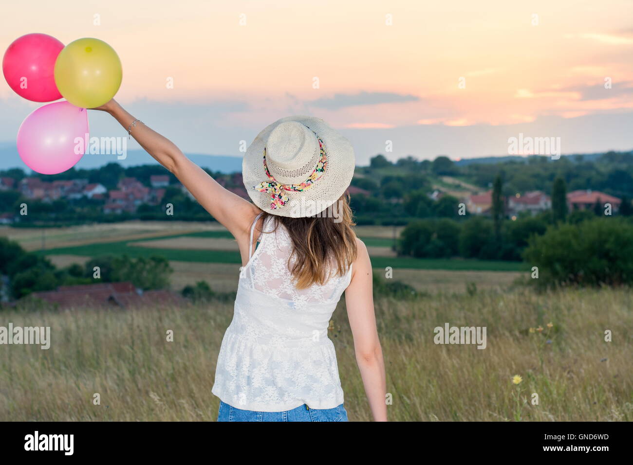 Giovane donna azienda palloncini e guardando il tramonto Foto Stock