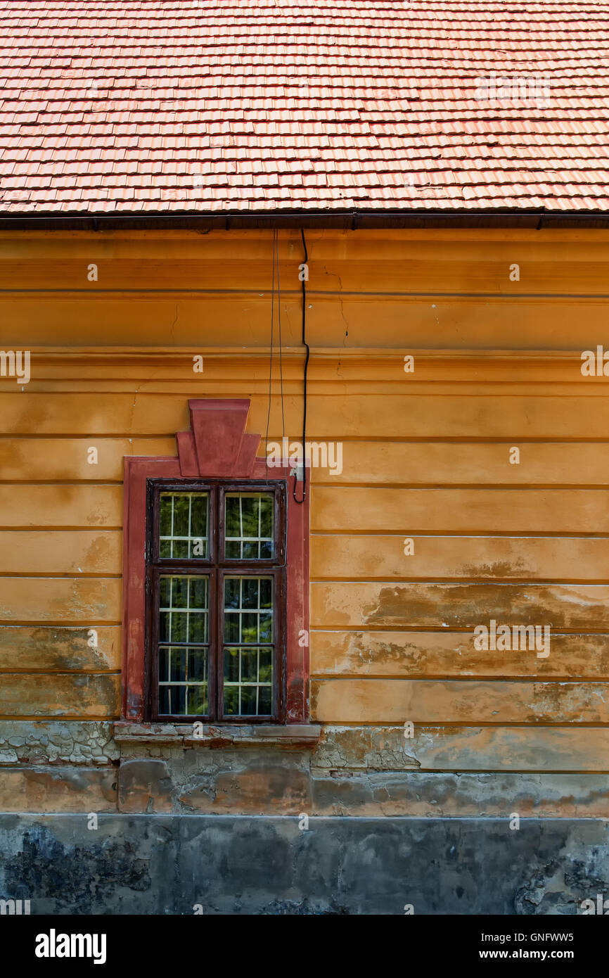 Vecchio muro di un abbandonato casa padronale con un elegante finestra. Parte di un tetto arancione. Foto Stock