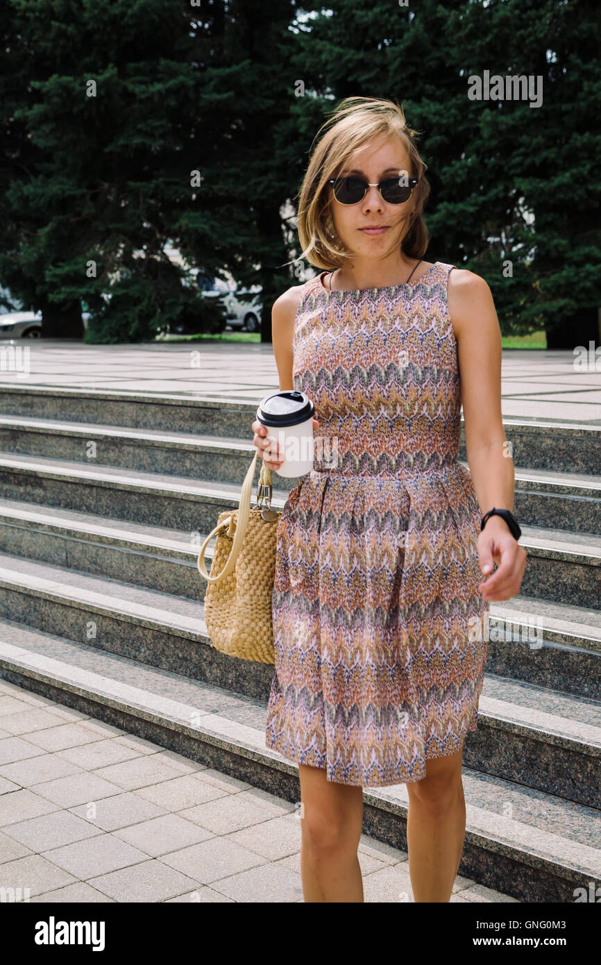 Donna elegante con caffè per andare a piedi verso il basso i passi in posizione di parcheggio Foto Stock