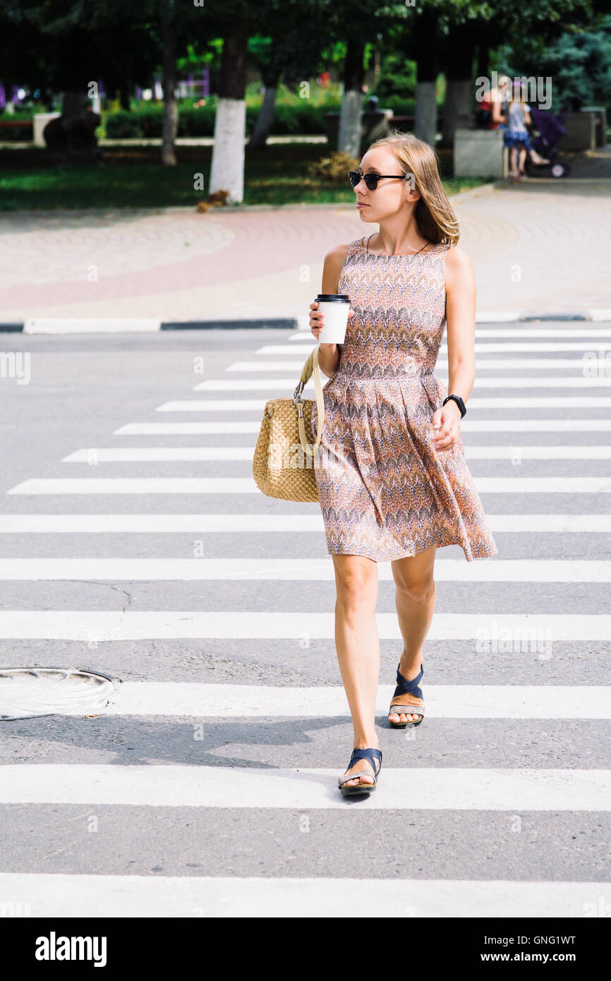 Bruna giovane donna in abito attraversando la strada con la tazza di caffè Foto Stock