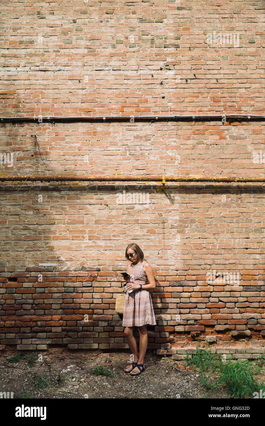 Giovane donna in abito con caffè di andare contro di brickwall Foto Stock