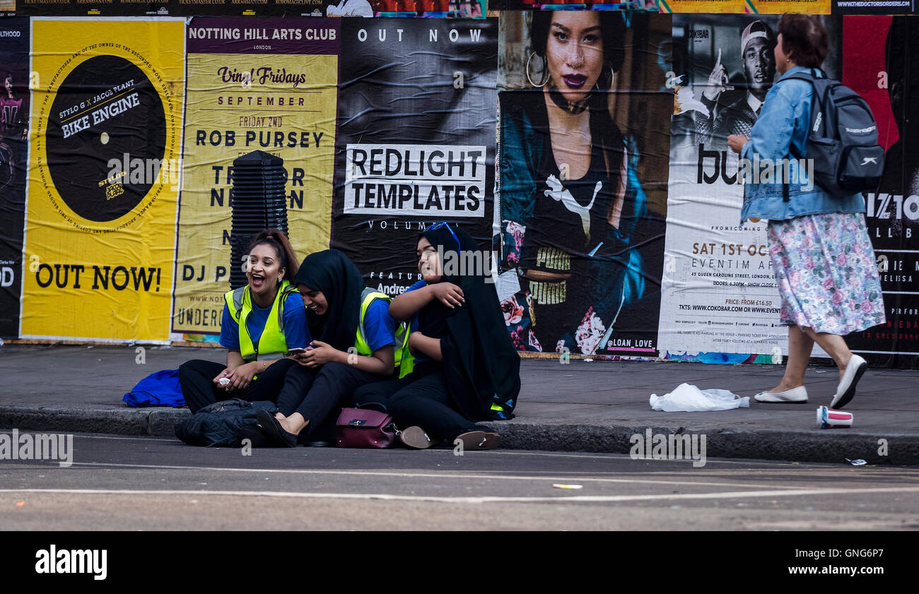 Carnevale di Notting Hill - 3 ragazze seduta ed avente una risata sul marciapiede in attesa per la folla di apparire. Foto Stock