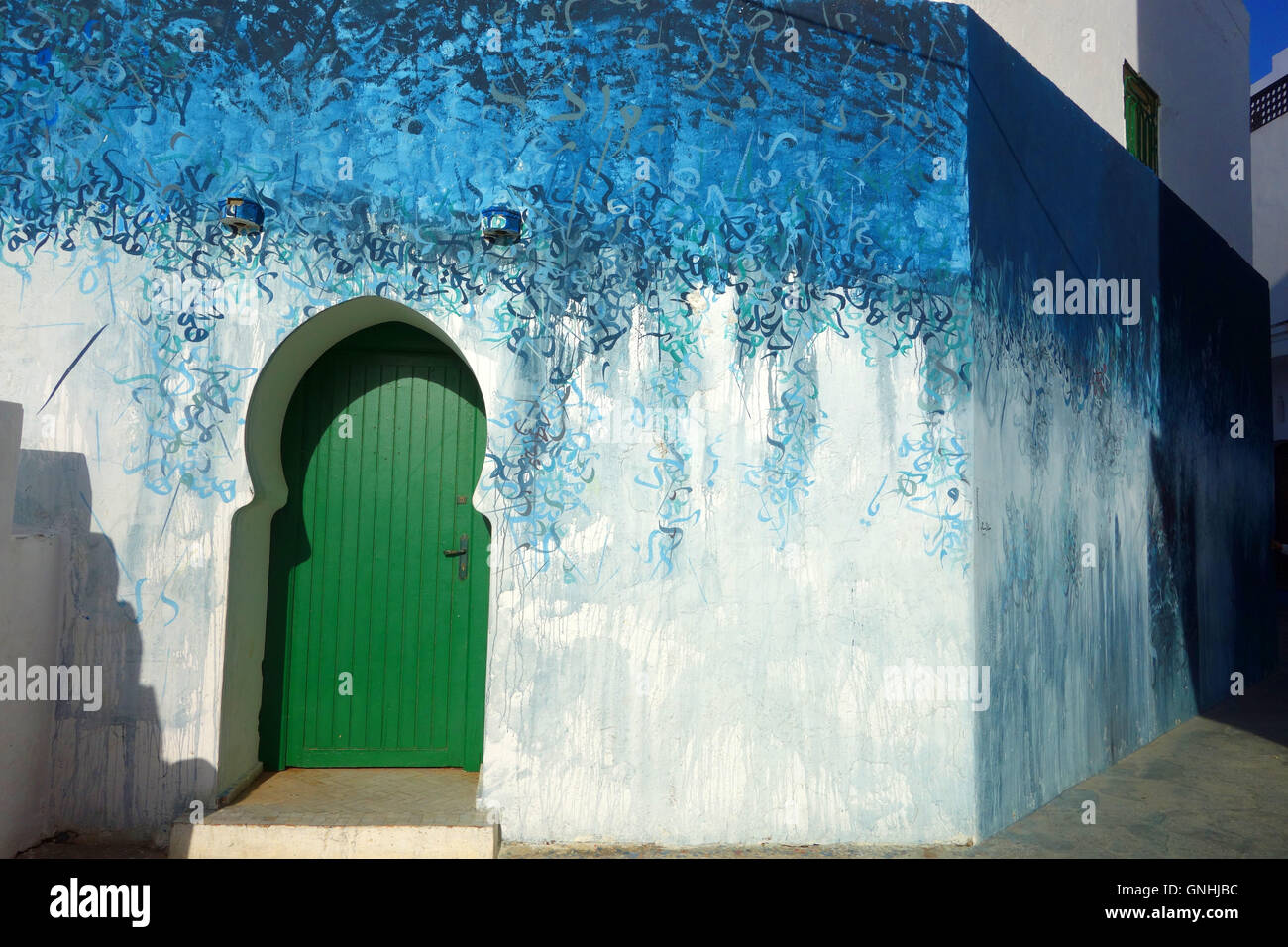 Marocchina di arte di strada con blu di scrittura araba e la porta verde in Alsirah, Marocco Foto Stock