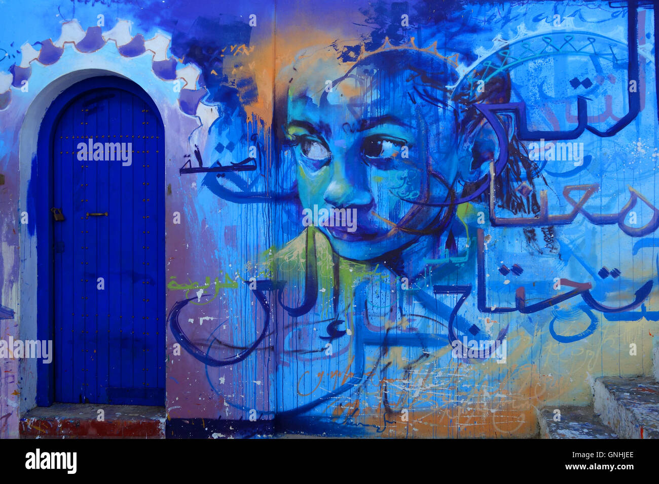 Marocchina di arte di strada di un bambino con una porta blu e scrittura araba in Alsirah, Marocco Foto Stock