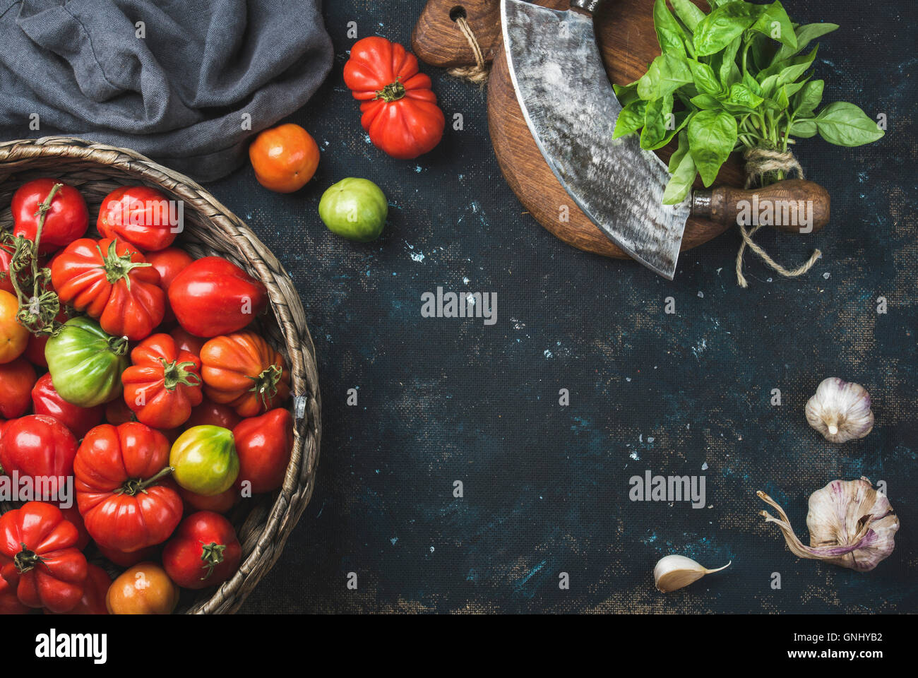 Fresh colorful ripe caduta cimelio di pomodori nel cestello, il verde del basilico in foglie, aglio ed erbe coltello del trinciapaglia per una cucina più sana o m Foto Stock