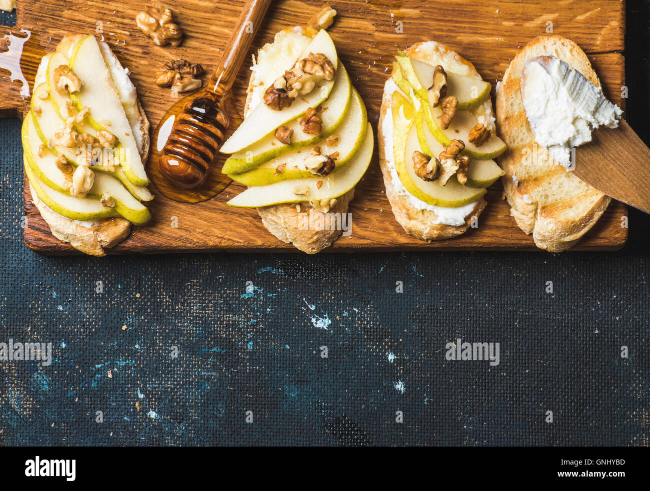 Crostini di pera, ricotta, miele e noci. La colazione toast o panini snack rustico di legno su blu scuro Foto Stock