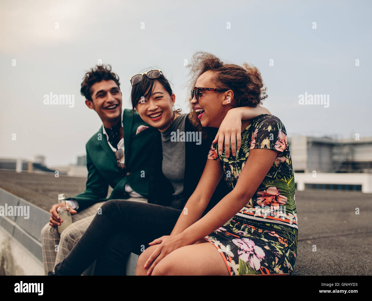 Colpo di felice giovani amici rilassante insieme sul tetto. Giovani uomini e donne seduti sulla terrazza e ridere. Foto Stock