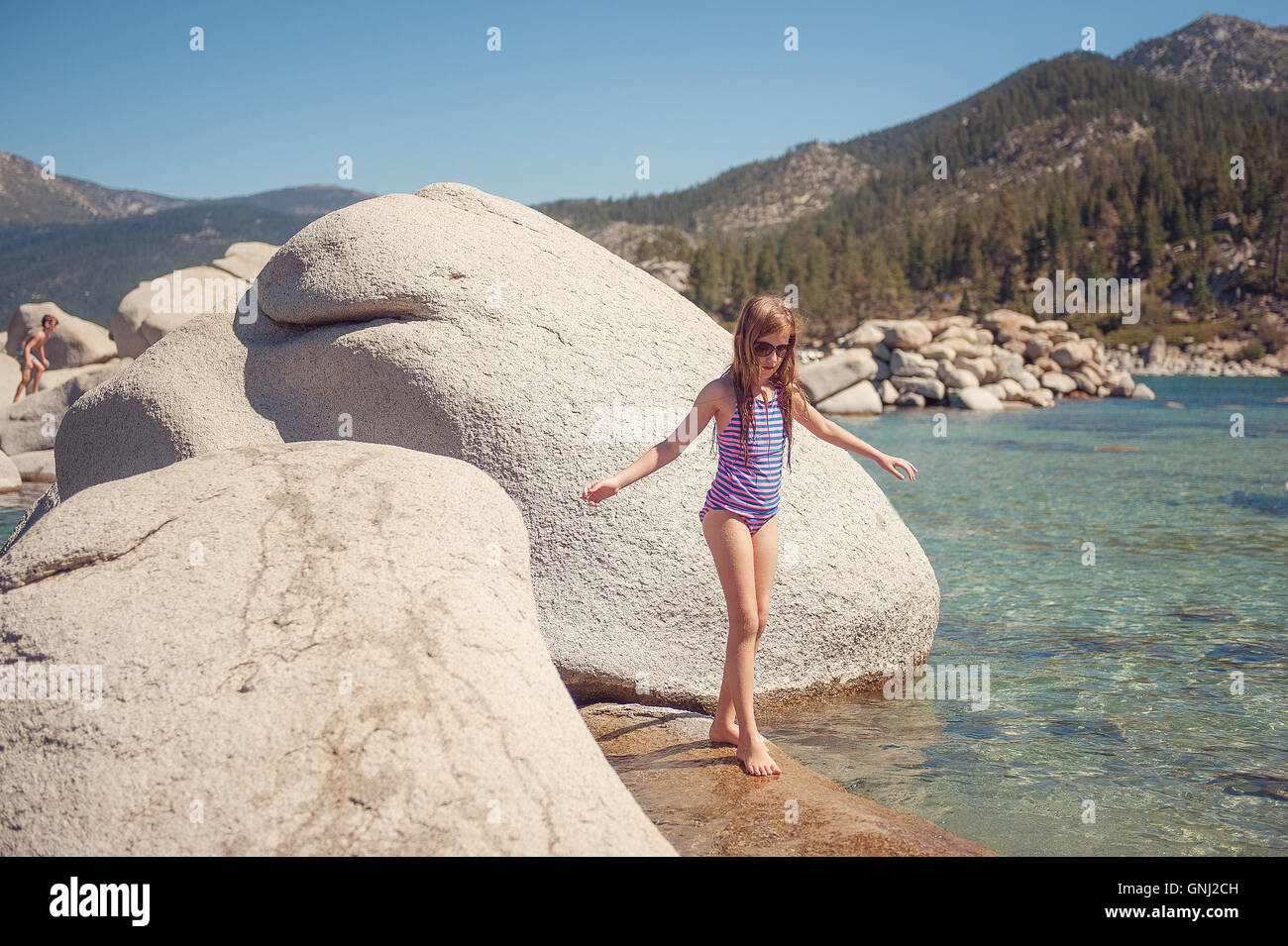 Ragazza in piedi su rocce con il fratello sullo sfondo il lago Tahoe, California, America, STATI UNITI D'AMERICA Foto Stock