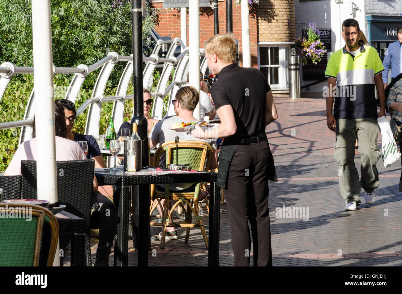 Un cameriere porta il cibo per un paio di diners che sono di mangiare all'aperto. Foto Stock