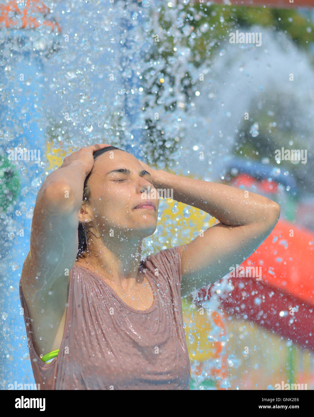 Bella donna godendo sotto un getto di acqua con migliaia di gocce in background Foto Stock