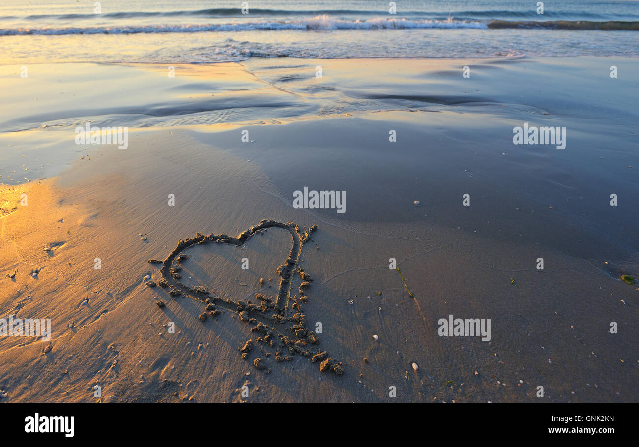 Disegno di un cuore su un giallo sabbia in un bellissimo paesaggio marino sfondo. Foto Stock