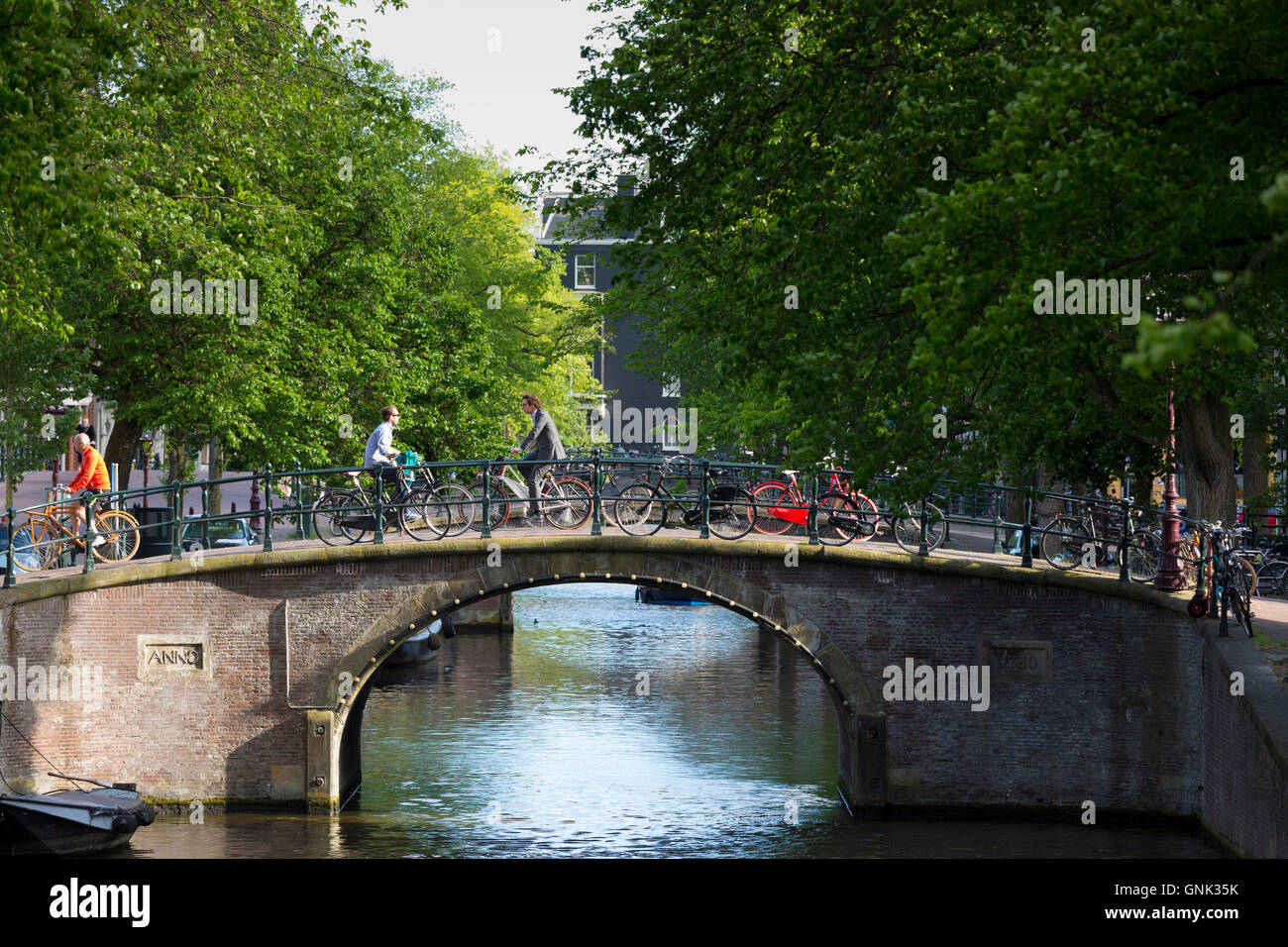 Canal e ciclisti attraversando uno dei Sette Ponti da angolo di Keizersgracht e Regilersgracht in Amsterdam, Olanda Foto Stock