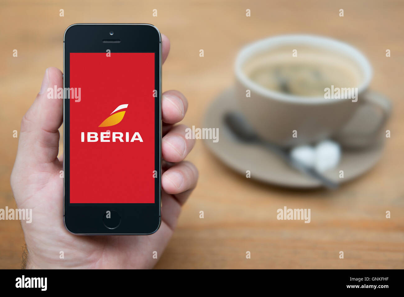 Un uomo guarda al suo iPhone che visualizza la compagnia aerea Iberia logo, mentre sat con una tazza di caffè (solo uso editoriale). Foto Stock