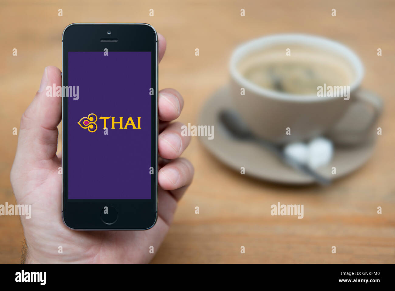 Un uomo guarda al suo iPhone che visualizza la Thai Airways logo, mentre sat con una tazza di caffè (solo uso editoriale). Foto Stock