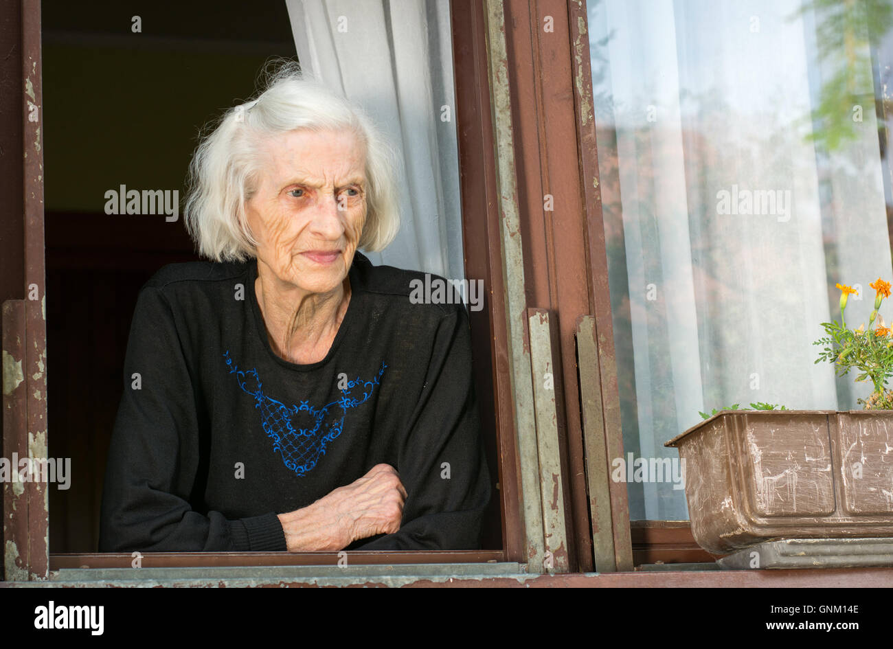 Senior donna solo sulla sua casa finestra Foto Stock