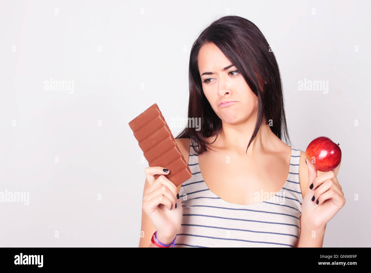 Giovane donna caucasica di effettuare una scelta tra cioccolato e Apple. Fitness e il concetto di dieta. Foto Stock