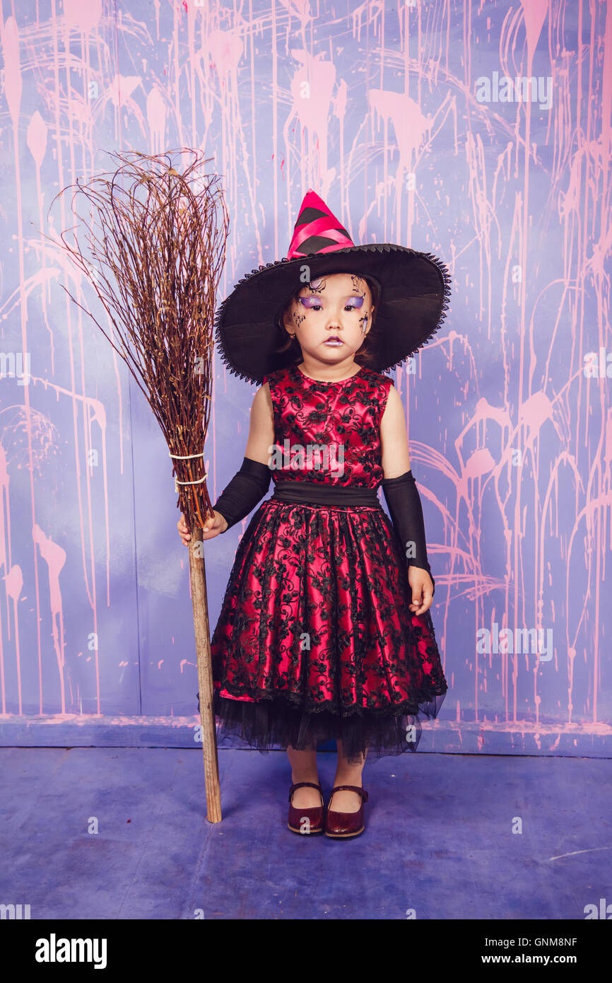 Una bambina vestita come una strega con una scopa in piedi su un sfondo di  parete viola Foto stock - Alamy