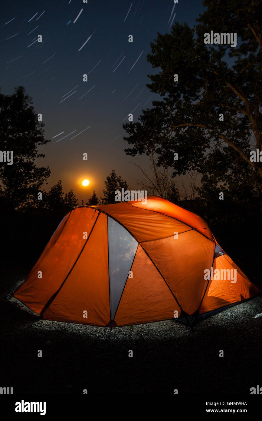 Una lunga esposizione di una tenda da campeggio di notte con la luna che sorge sull'orizzonte e sentieri a stella nel firmamento. Foto Stock