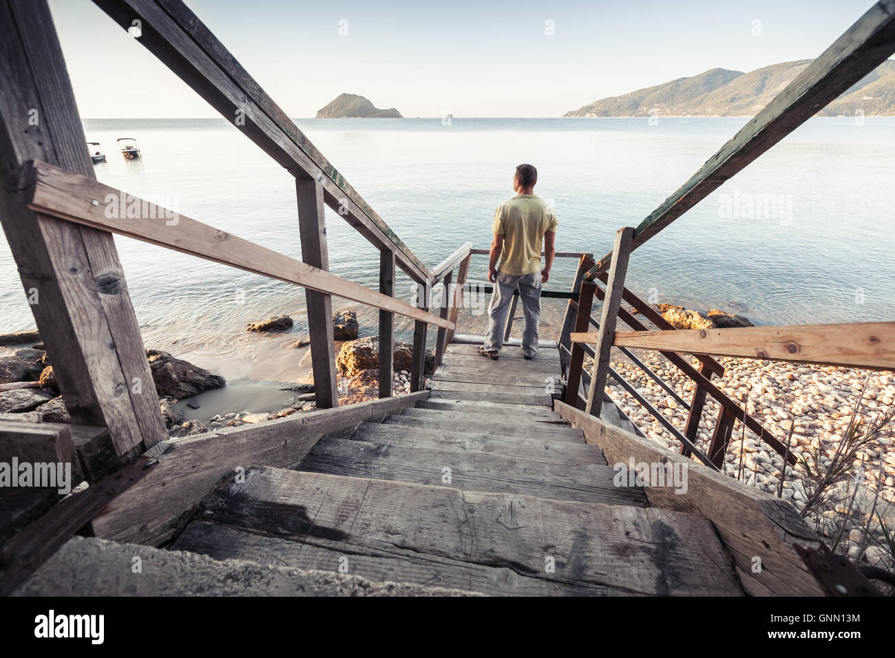 Giovane uomo sorge su una vecchia scala di legno andando giù per la costa del mare al mattino Foto Stock