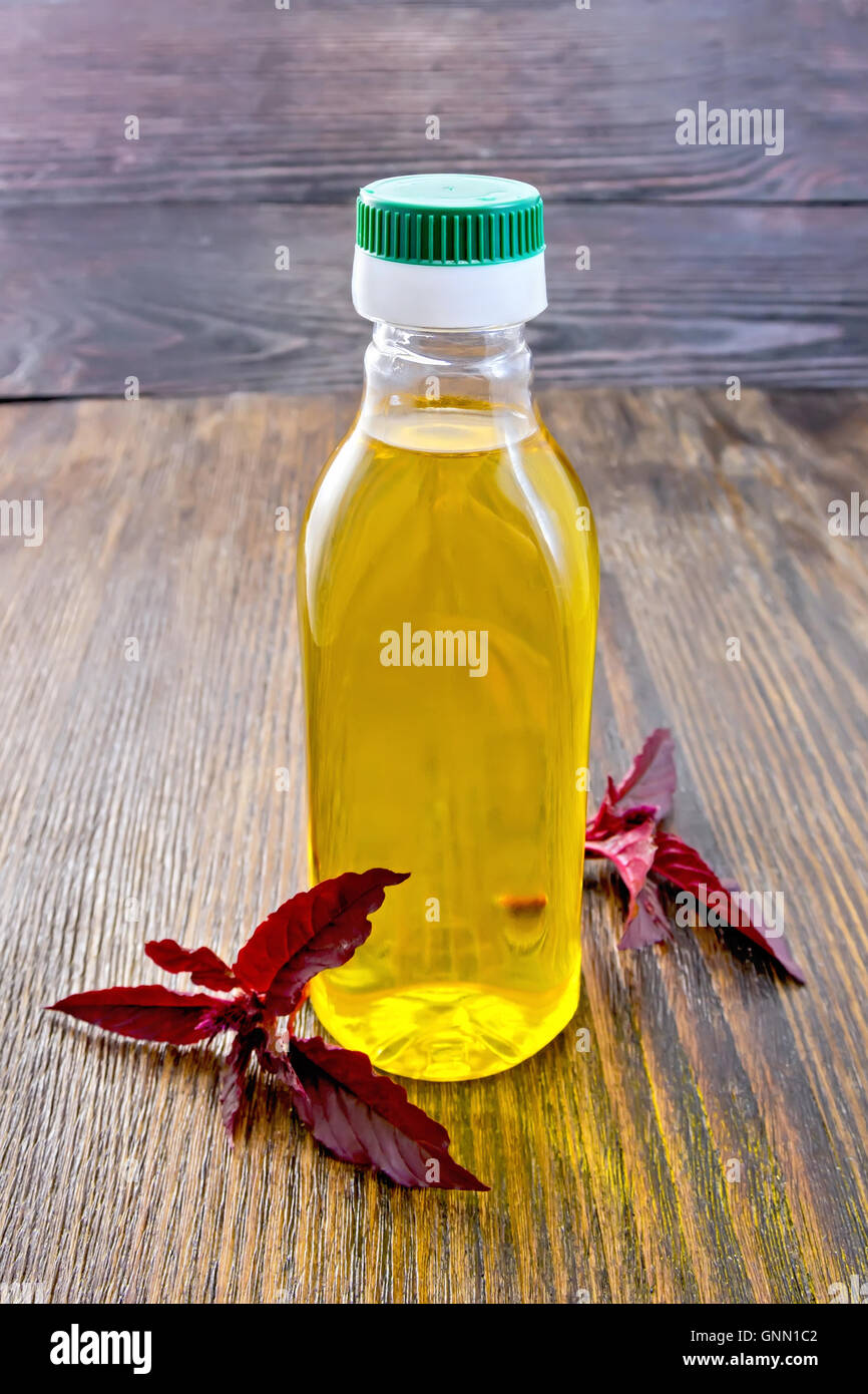 Una bottiglia di plastica di olio con un ramo di amaranto Borgogna al buio su un pannello di legno Foto Stock