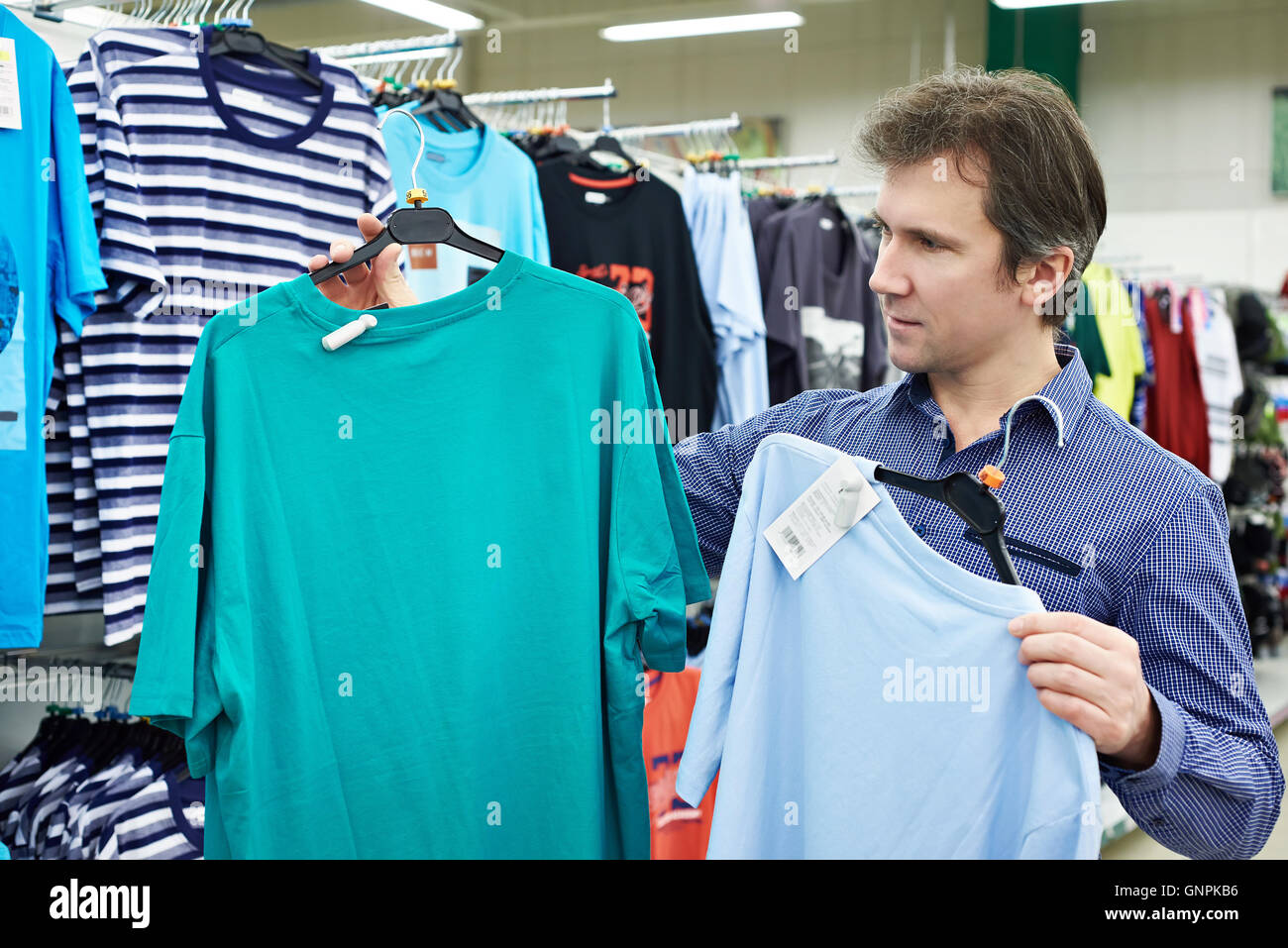 Uomo sceglie una t-shirt in negozio Foto Stock
